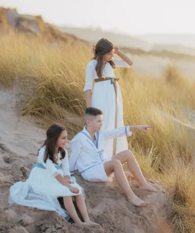 Dos niñas y un niño vestidos de comunión en la playa