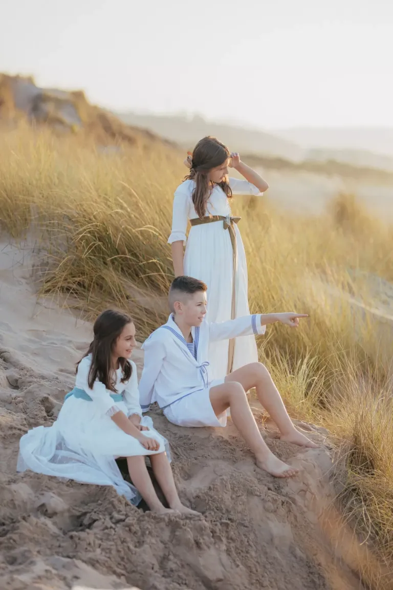 Dos niñas y un niño vestidos de comunión en la playa