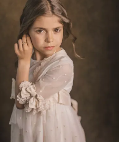 Niña vestida de comunión tocándose la oreja