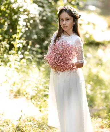 Niña vestida con traje de comunión en el campo sujetando un ramo de flores