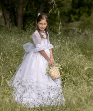 Niña vestida de comunión con una cesta de flores en el campo