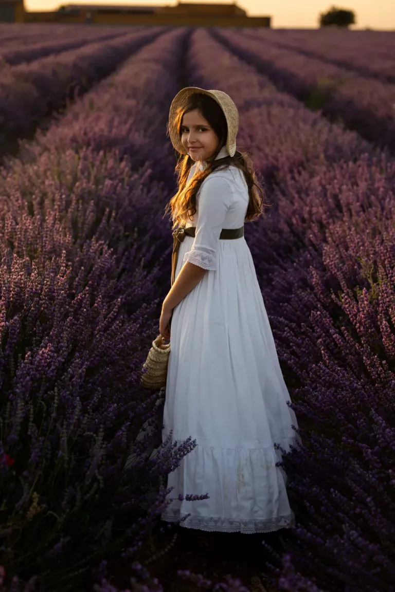 Niña vestida de comunión en un campo con flores violetas