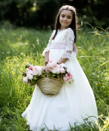 Niña vestida de comunión con una cesta de flores en el campo