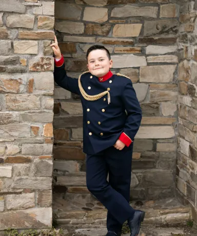 Niño vestido de comunión apoyado en una pared de ladrillo