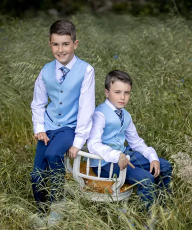 Dos niños vestidos con traje de comunión en una silla