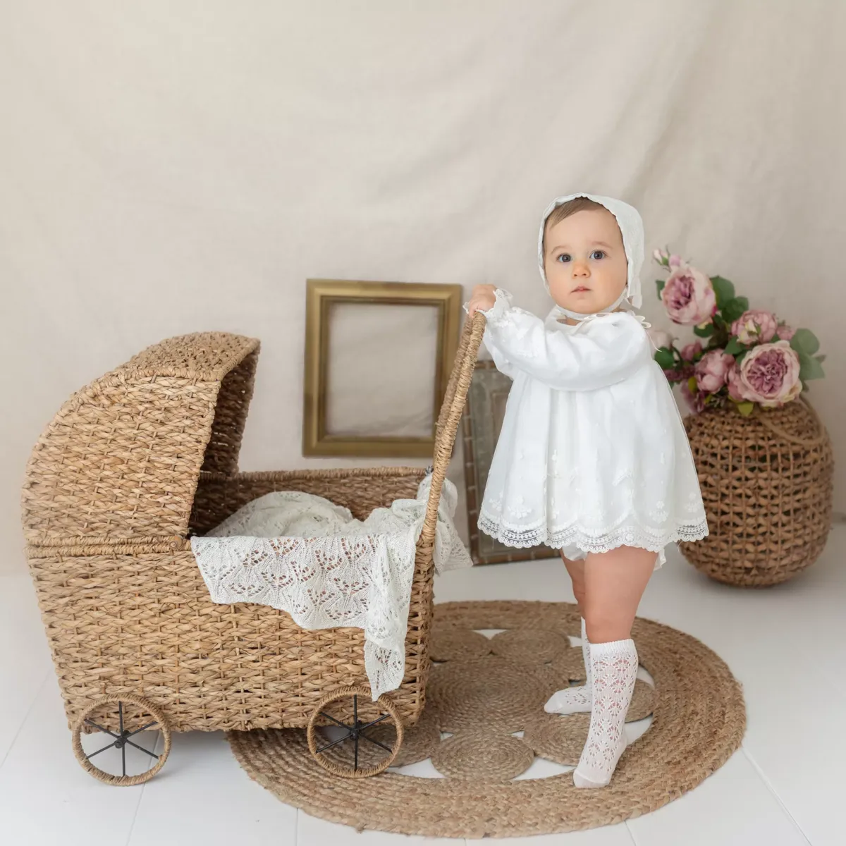 Niña con vestido blanco sujetando un carricoche de mimbre