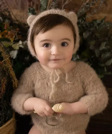 Bebé vestido con body y gorro de lana junto a varias plantas