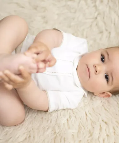 Niño cogiéndose los pies con las manos tumbado en una manta